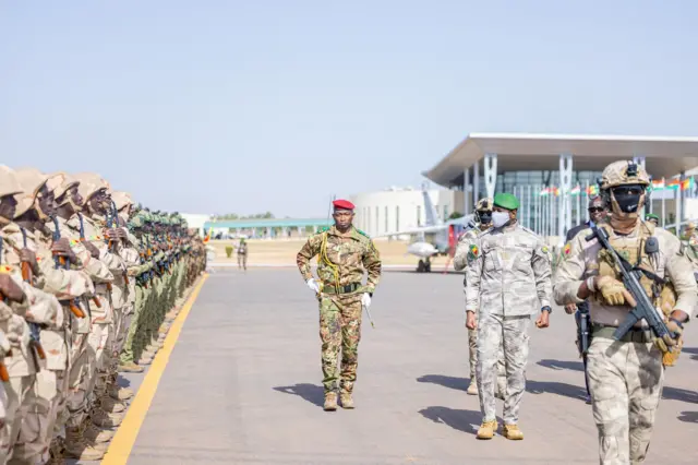 Le général Assimi Goïta, président de la transition au Mali, inspecte des troupes en tenue militaire avec béret vert et cache-nez.