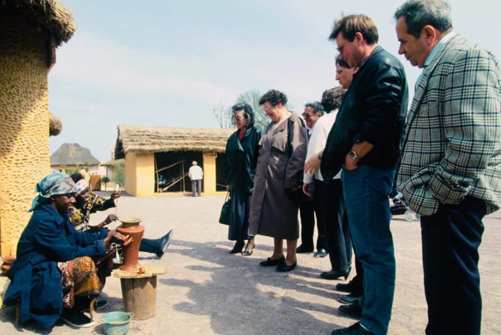 Groupe de personnes devant des cases traditionnelles dans un parc